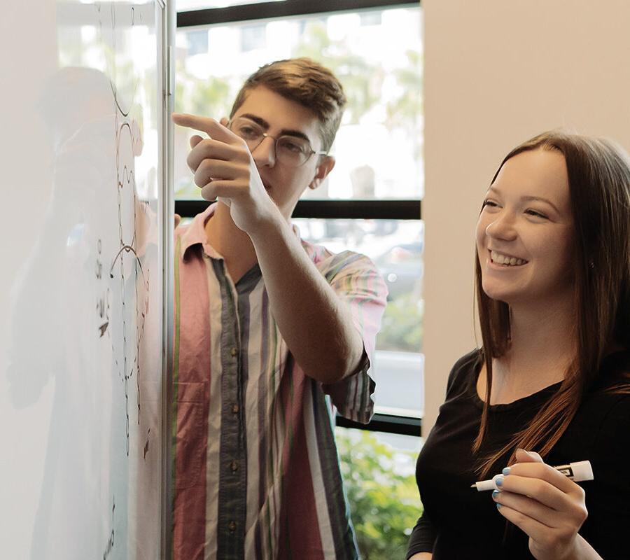 Two PBA students draw diagrams on a whiteboard.